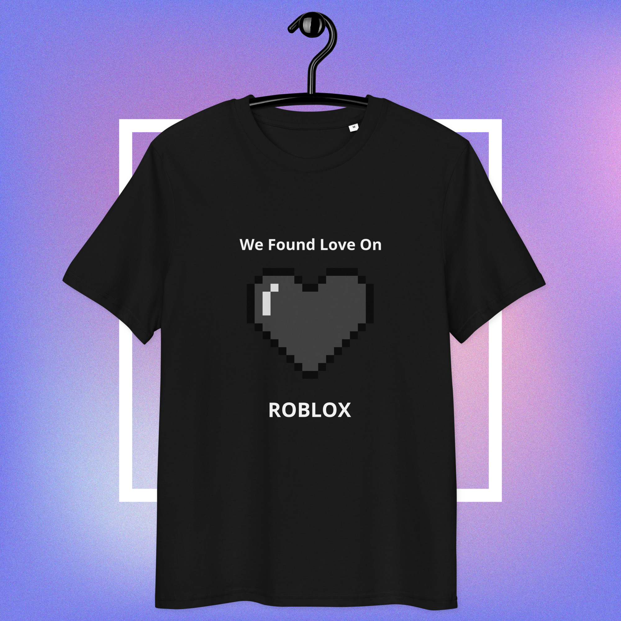 A black short-sleeve t-shirt hanging on a black hanger against a purple and blue gradient background with a white geometric frame. The shirt features a pixelated dark gray heart graphic with a small white highlight, accompanied by the white text 'We Found Love On' above and 'ROBLOX' below.
